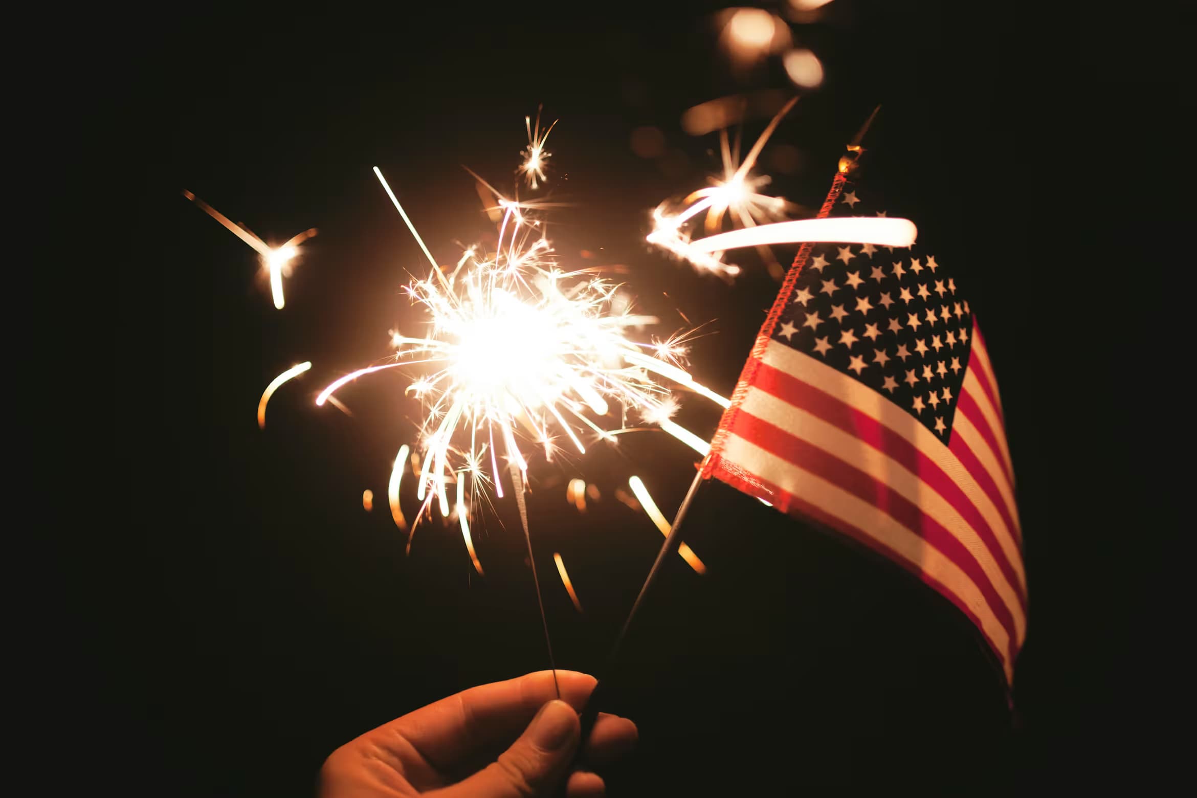 A hand holding a sparkler and an American flag